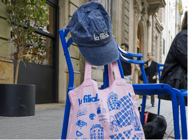 Gorra y tote bag de La Filial sobre una silla en la calle